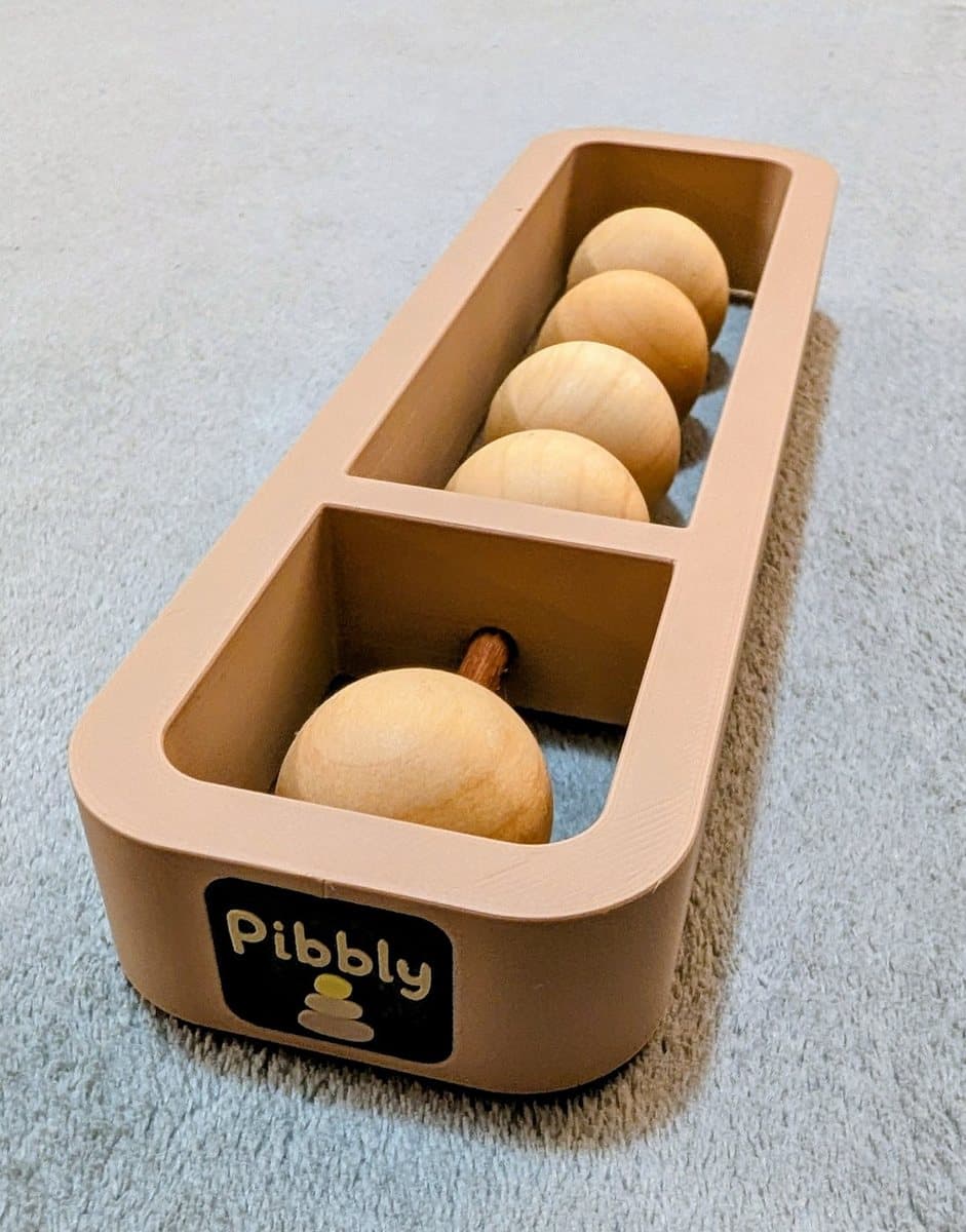 A Pibbly single-rod soroban resting on a rug, its clay-coloured frame carrying the Pibbly logo, with four wooden beads in the long compartment and one in a compartment of its own.