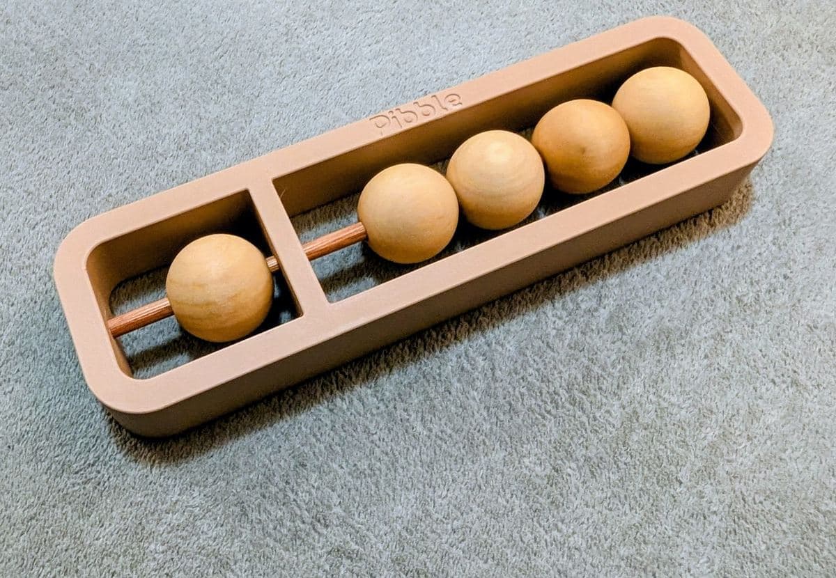 The Pibble, Pibbly's single-rod soroban, photographed from above: a clay-coloured frame holding one wooden bead in a small compartment of its own and four wooden beads in the long compartment beside it.